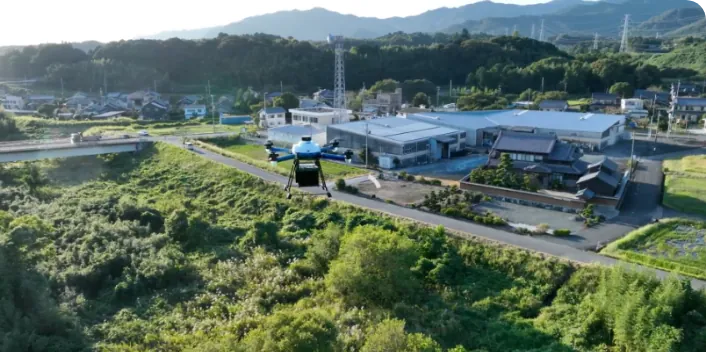 Drone hovering over a rural village with a warehouse, houses and rice fields